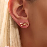 Model wearing simple ribbon stud earrings in 14k gold, showcasing their playful and elegant bow style.
