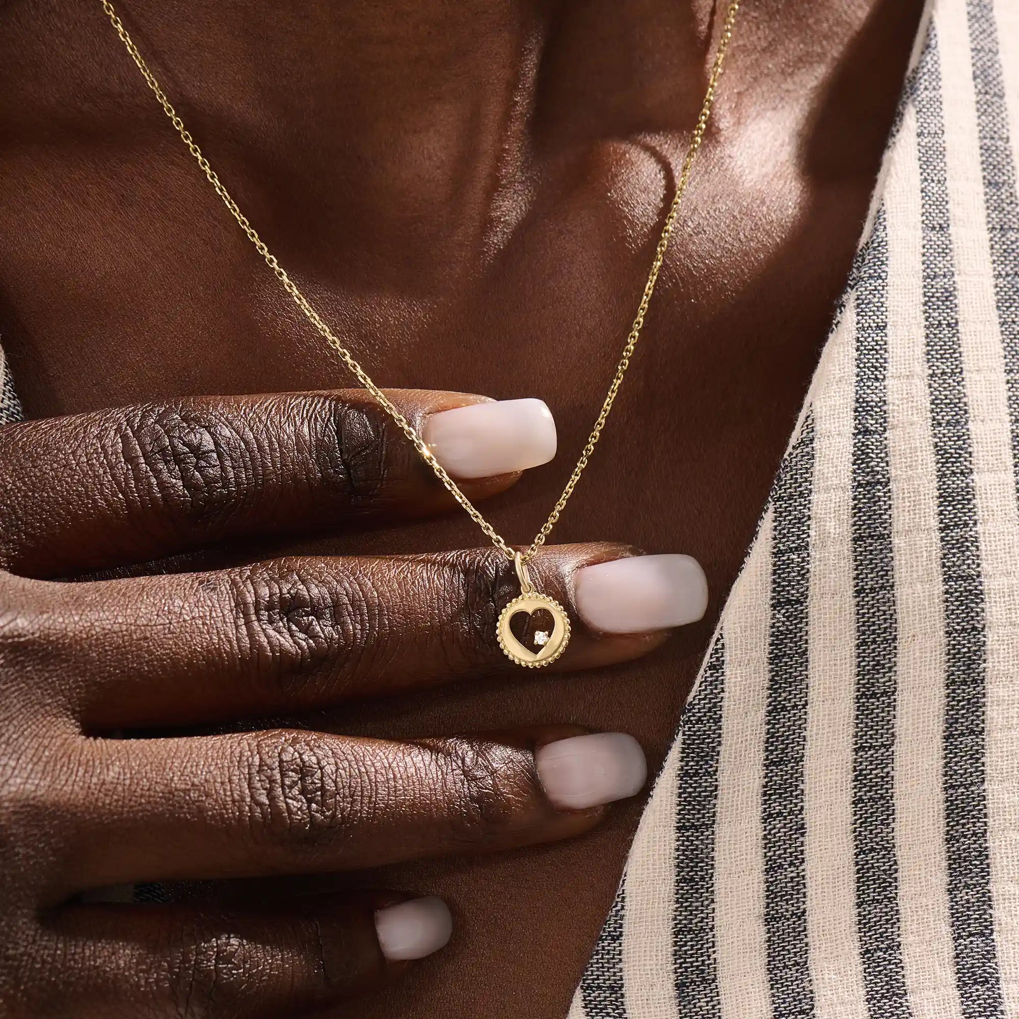 Model wears a 14k gold circle pendant necklace with a heart cutout and single moissanite accent. A minimalist and elegant everyday piece.