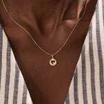 Model wears a 14k gold circle pendant necklace with a heart cutout and single moissanite accent. A minimalist and elegant everyday piece.