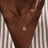 Model wears a 14k gold circle pendant necklace with a heart cutout and single moissanite accent. A minimalist and elegant everyday piece.