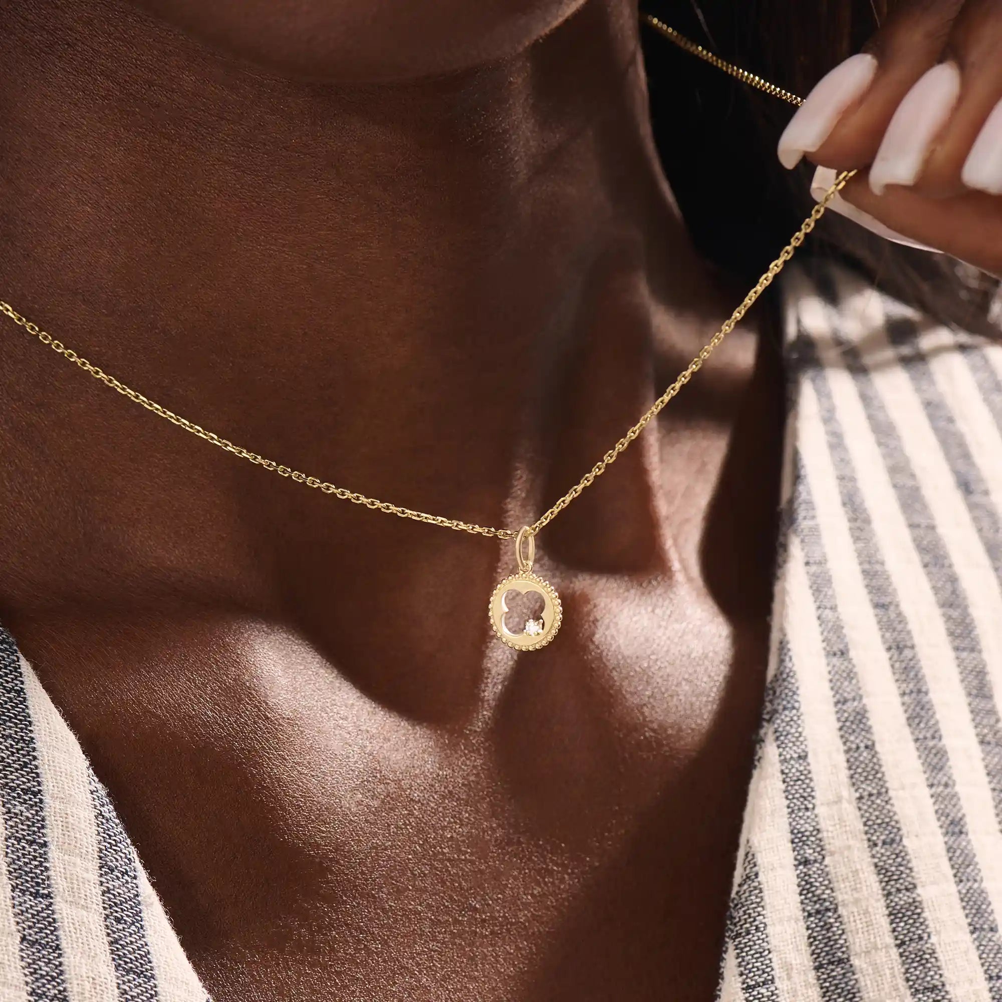 Model wears a 14k gold circle pendant necklace with clover cutout and single moissanite accent. A minimalist and meaningful everyday accessory.