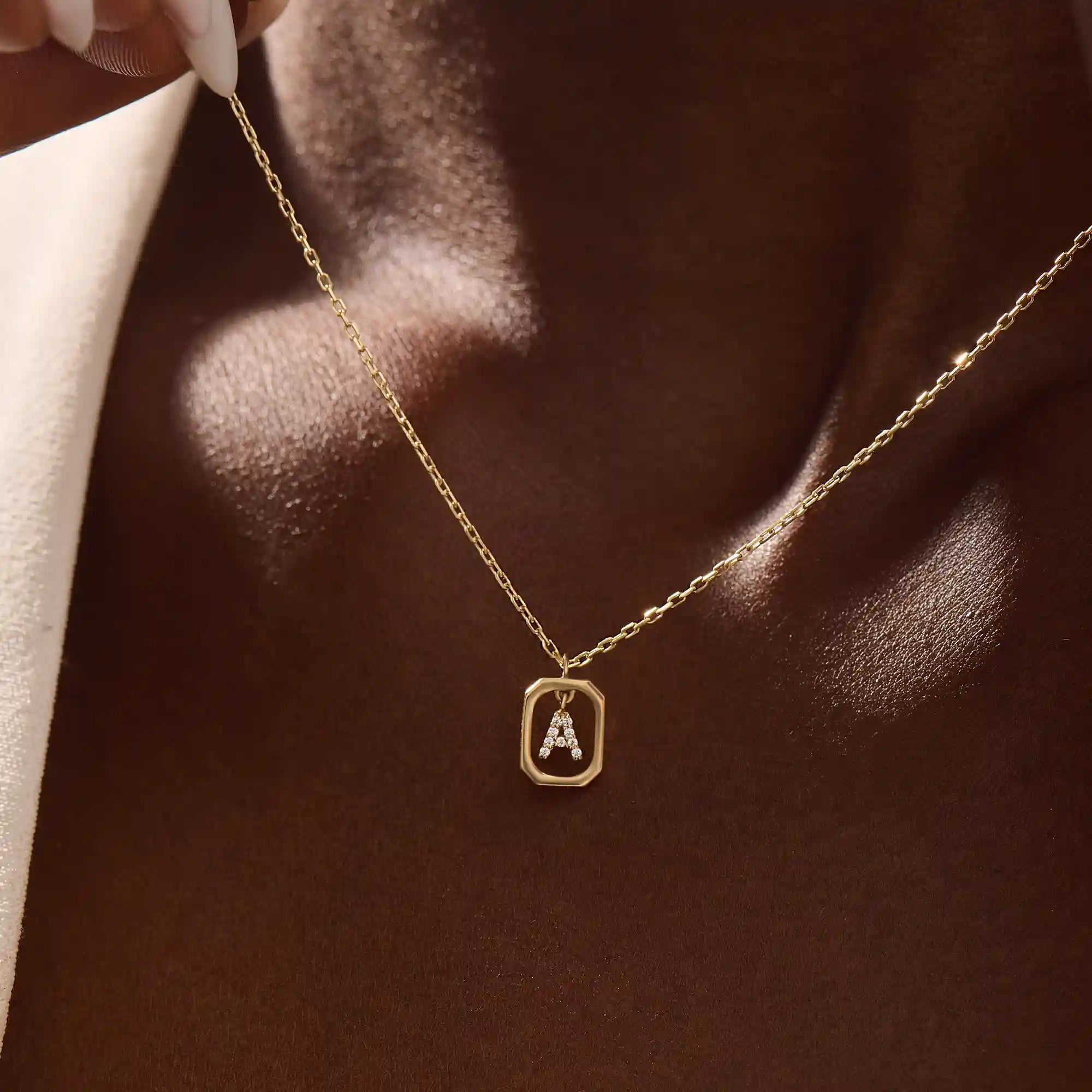 Model wears a 14k gold rectangle necklace with a dangling personalized letter charm. Sleek and meaningful jewelry perfect for layering.