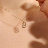Model wears a 14k gold rectangle necklace with a dangling personalized letter charm. Sleek and meaningful jewelry perfect for layering.