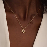 Model wears a 14k gold rectangle necklace with a dangling personalized letter charm. Sleek and meaningful jewelry perfect for layering.