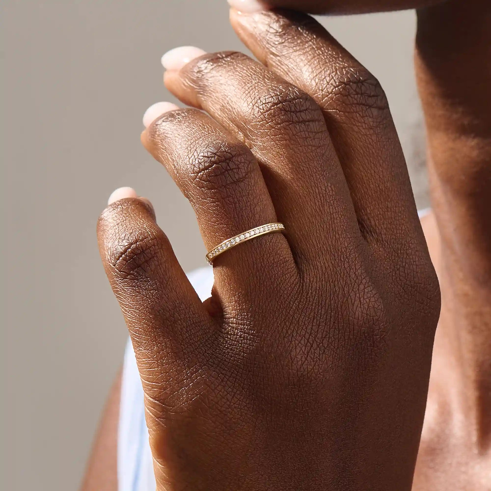 Model wears a 14k gold two-sided wedding ring featuring leaf engravings and channel-set moissanites. Perfect for a distinctive and meaningful wedding band.