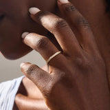 Model wears a 14k gold two-sided wedding ring featuring leaf engravings and channel-set moissanites. Perfect for a distinctive and meaningful wedding band.