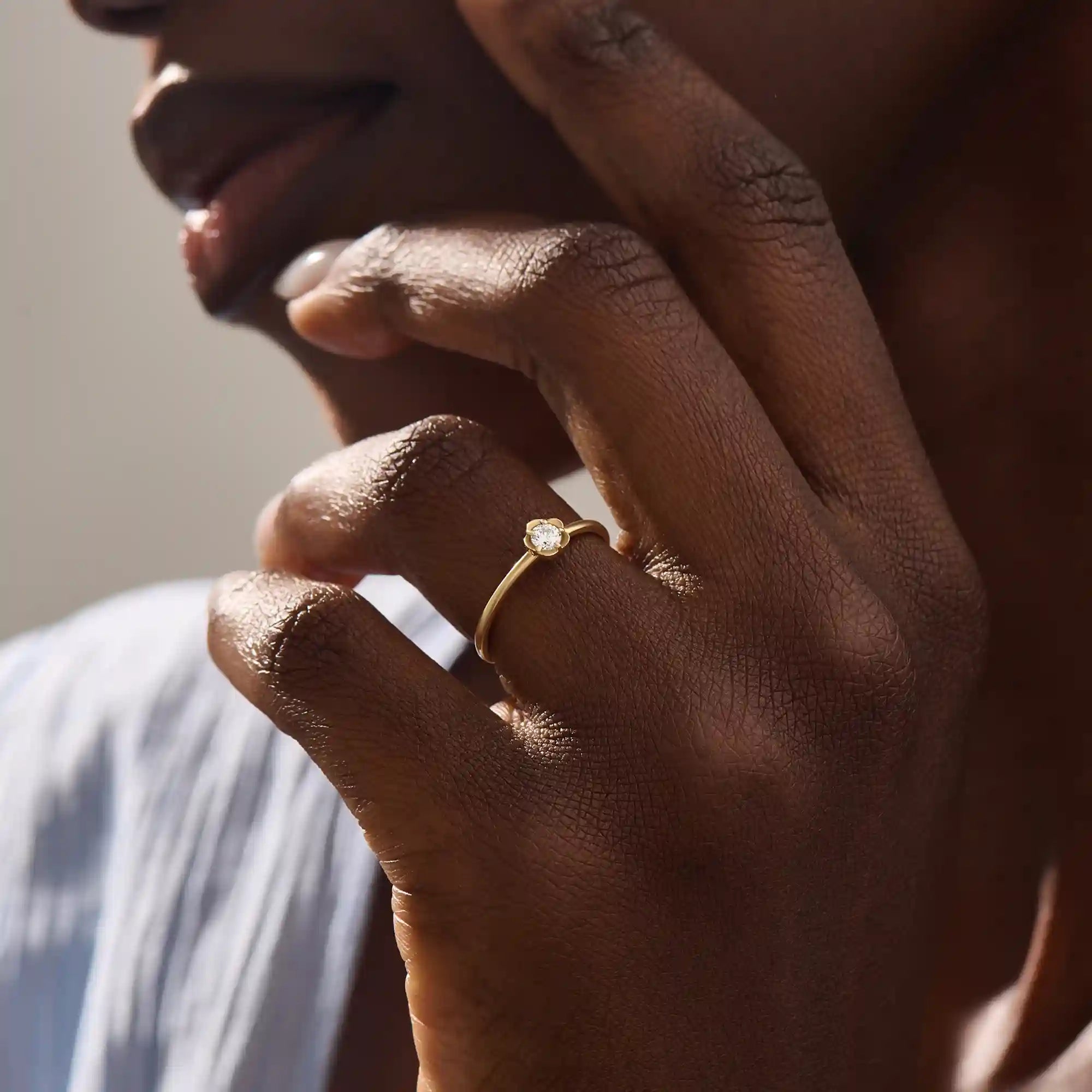 Model wears a 14k solid gold solitaire engagement or promise ring with a small flower motif. Elegant and subtle design for women’s daily wear or special occasions.