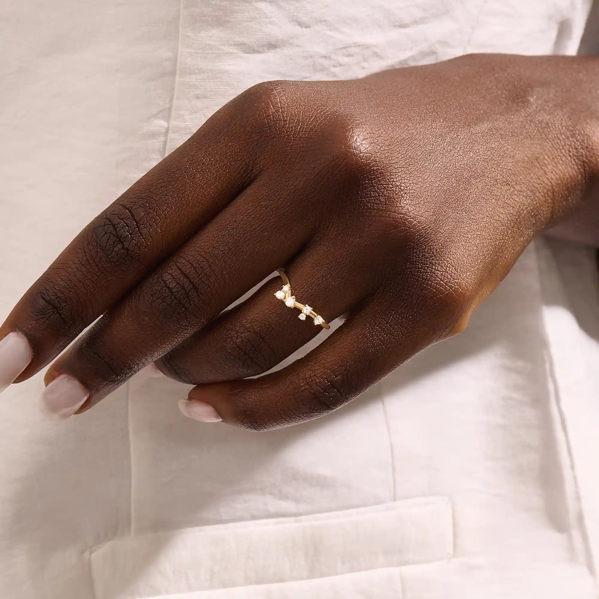 Model wears a curved 14k gold nesting ring with scattered moissanites. A delicate stacking piece that adds soft brilliance to any ring stack.