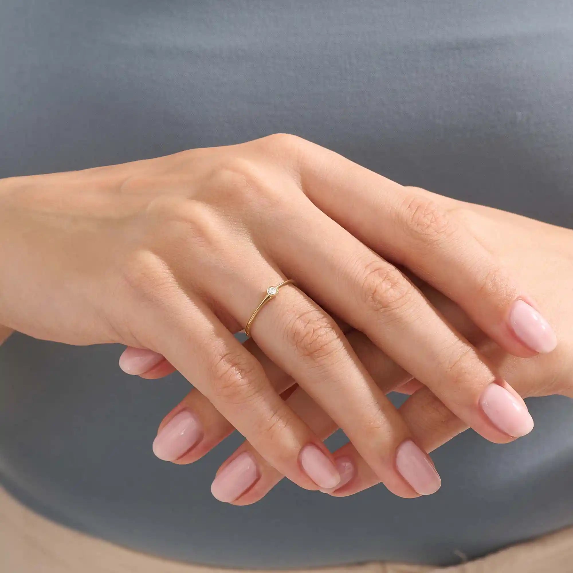 Model wears a simple 14k gold promise ring featuring a small bezel-set moissanite. A subtle and elegant symbol of commitment.