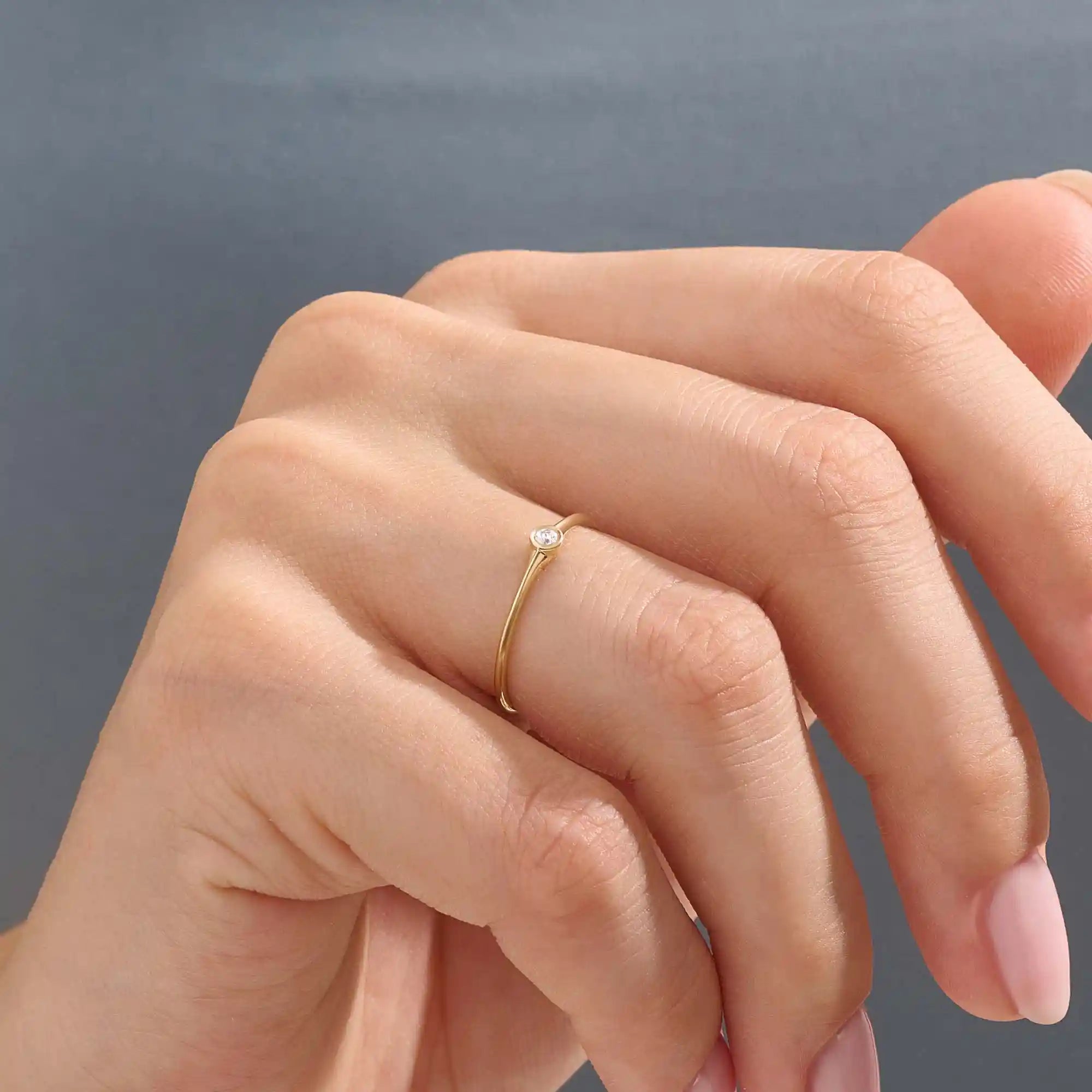 Model wears a simple 14k gold promise ring featuring a small bezel-set moissanite. A subtle and elegant symbol of commitment.