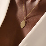 Model wears an oval plain pendant necklace in 14k gold, ideal for personal engravings. A sleek and versatile everyday accessory.