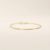 Side angle of a 14k solid yellow gold flat bar chain bracelet, showing the slim rectangular links and the light-catching polished finish.
