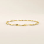 Side angle of a 14k solid yellow gold twist bangle bracelet, highlighting its smooth wave-like curves and reflective surface.
