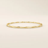 Side angle of a 14k solid yellow gold twist bangle bracelet, highlighting its smooth wave-like curves and reflective surface.

