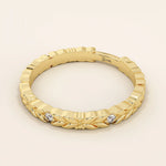 Side angle view of a 14k solid yellow gold band with laurel leaf design and bezel set round brilliant cut moissanite stones, refined and unique bridal jewelry
