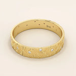 Side angle view of a 14k solid yellow gold wedding band with a concentric circle pattern and bezel-set round moissanites, bold geometric style
