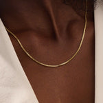Woman wearing a 14k solid gold box chain necklace with sleek, structured links. Minimalist and versatile gold chain for everyday styling. Perfect on its own or with other pieces.