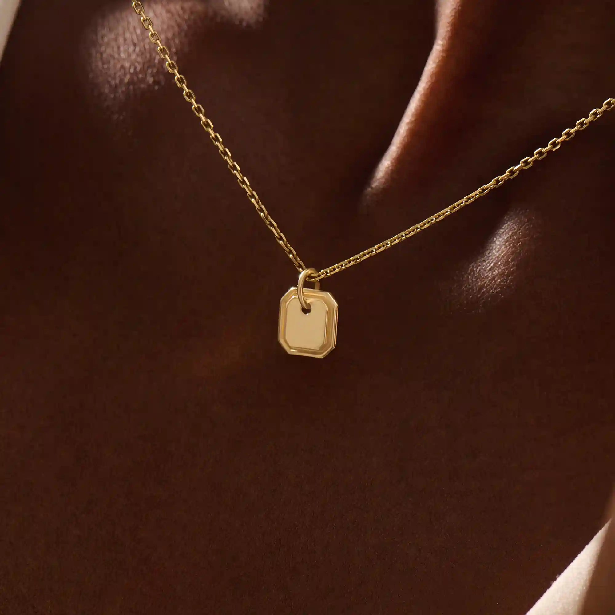 Woman wearing a 14k solid gold dainty octagon pendant necklace. Lightweight and easy-to-style gold charm. Perfect for daily looks or as a layering piece.