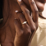 Woman wearing a 14k solid gold engagement ring with a round moissanite and small side accents. A subtle and elegant ring for everyday wear. Ideal for those who love classic, refined style.