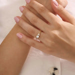 Woman wearing a 14k solid gold engagement ring with a round moissanite and small side accents. A subtle and elegant ring for everyday wear. Ideal for those who love classic, refined style.