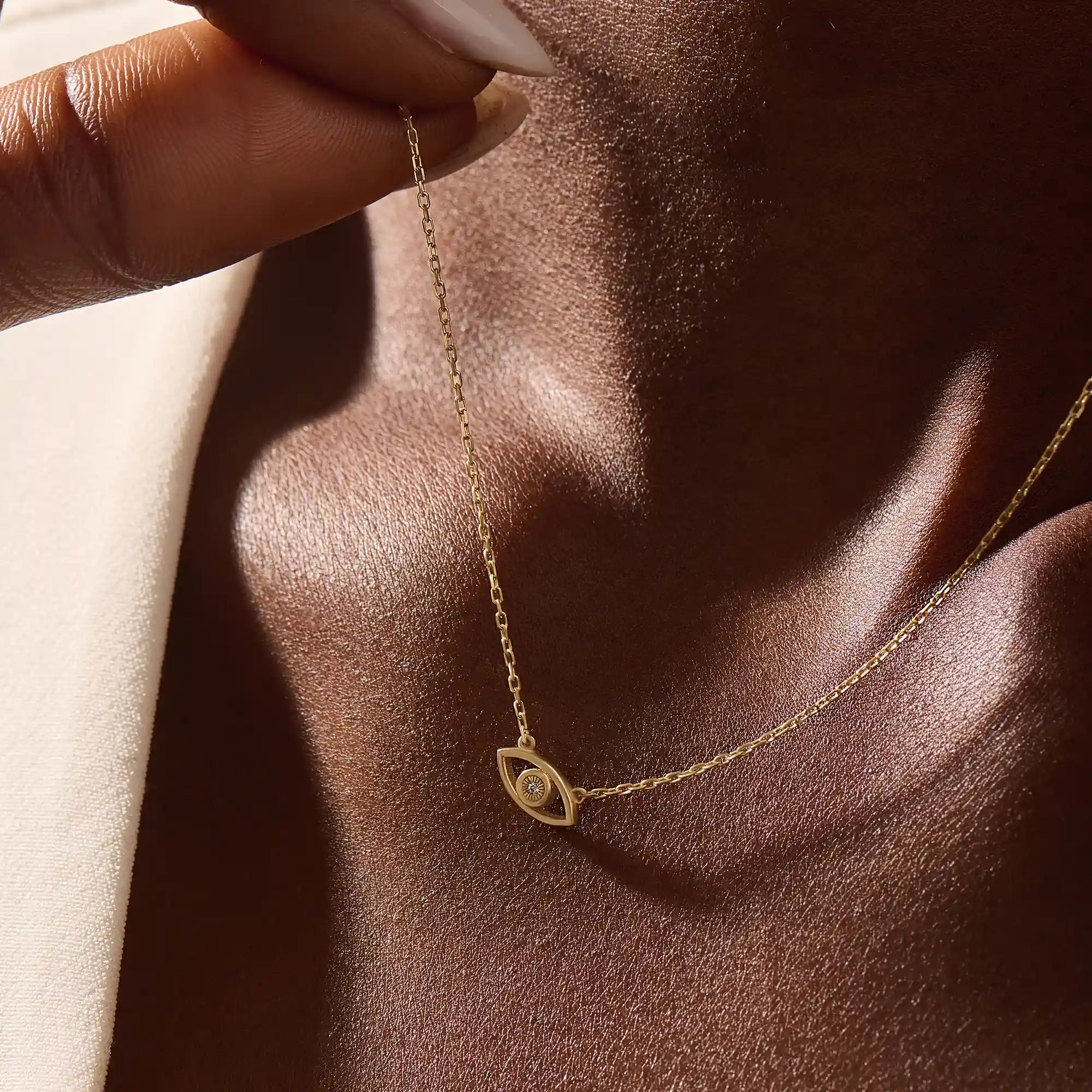 Woman wearing a 14k solid gold evil eye necklace resting at the collarbone. A symbolic and dainty gold design for daily style. Great for layering or wearing solo.
