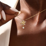 Woman wearing a 14k solid gold flower necklace with five petals and a sparkling dangling moissanite. Nature-inspired and graceful gold jewelry. Perfect for soft, romantic styling.