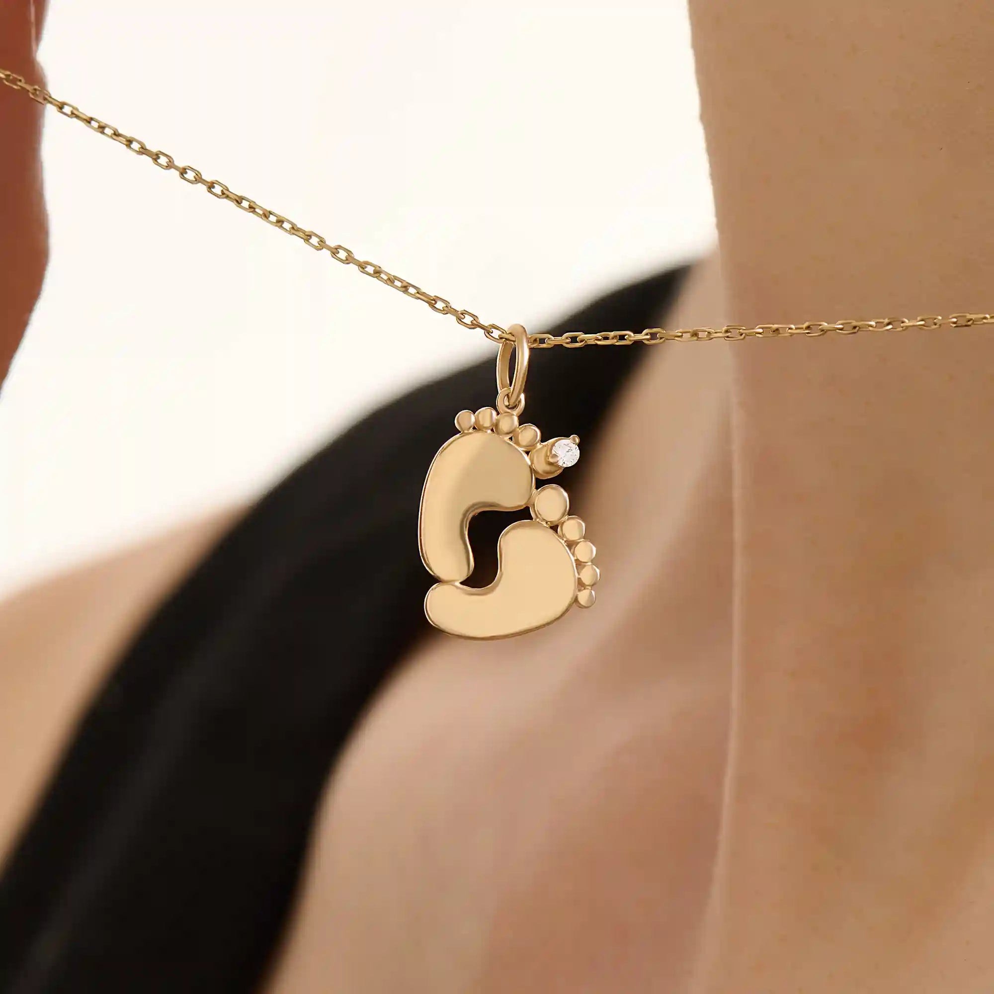 Woman wearing a 14k solid gold necklace with a baby foot pendant and sparkling moissanite detail. A meaningful and dainty gold piece celebrating motherhood and love. Ideal for layering or as a daily keepsake.