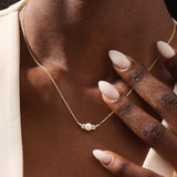 Woman wearing a 14k solid gold pearl necklace with sparkling moissanite clusters flanking the center pearl. Chic and refined gold necklace for women. Great for layering or special occasions.