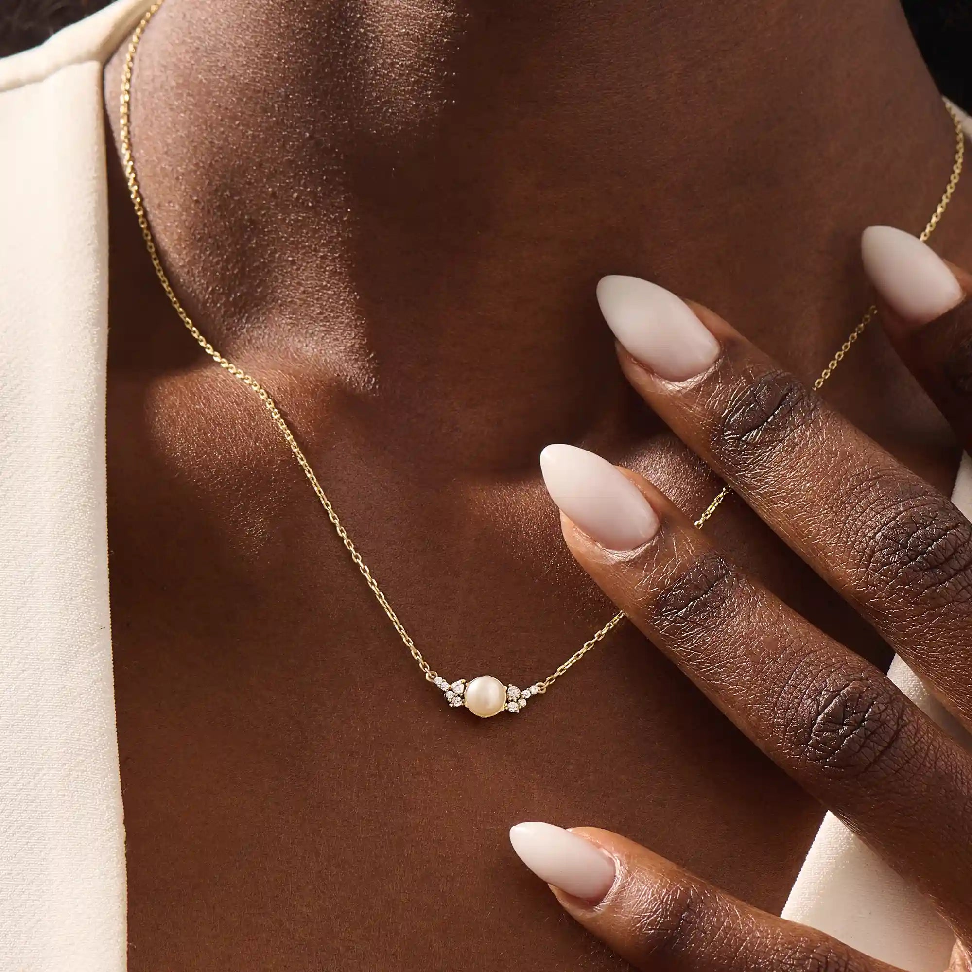 Woman wearing a 14k solid gold pearl necklace with sparkling moissanite clusters flanking the center pearl. Chic and refined gold necklace for women. Great for layering or special occasions.