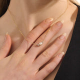 Woman wearing a 14k solid gold pearl necklace with sparkling moissanite clusters flanking the center pearl. Chic and refined gold necklace for women. Great for layering or special occasions.