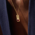 Woman wearing a 14k solid gold rectangle pendant necklace featuring an emerald-cut lab-created ruby in bezel setting. Striking birthstone jewelry with timeless elegance. Ideal for everyday wear or special occasions.