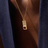 Woman wearing a 14k solid gold rectangle pendant necklace featuring an emerald-cut lab-created ruby in bezel setting. Striking birthstone jewelry with timeless elegance. Ideal for everyday wear or special occasions.