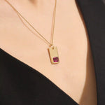 Woman wearing a 14k solid gold rectangle pendant necklace featuring an emerald-cut lab-created ruby in bezel setting. Striking birthstone jewelry with timeless elegance. Ideal for everyday wear or special occasions.