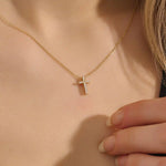 Woman wearing a 14k solid gold reversible cross necklace with pave moissanites on both sides. Subtle and elegant everyday jewelry. Designed for modern layering looks.