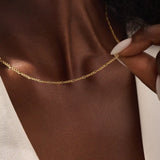 Woman wearing a 14k solid gold slim Figaro chain necklace with a delicate, timeless link pattern. Subtle and elegant for everyday styling. Great on its own or stacked.