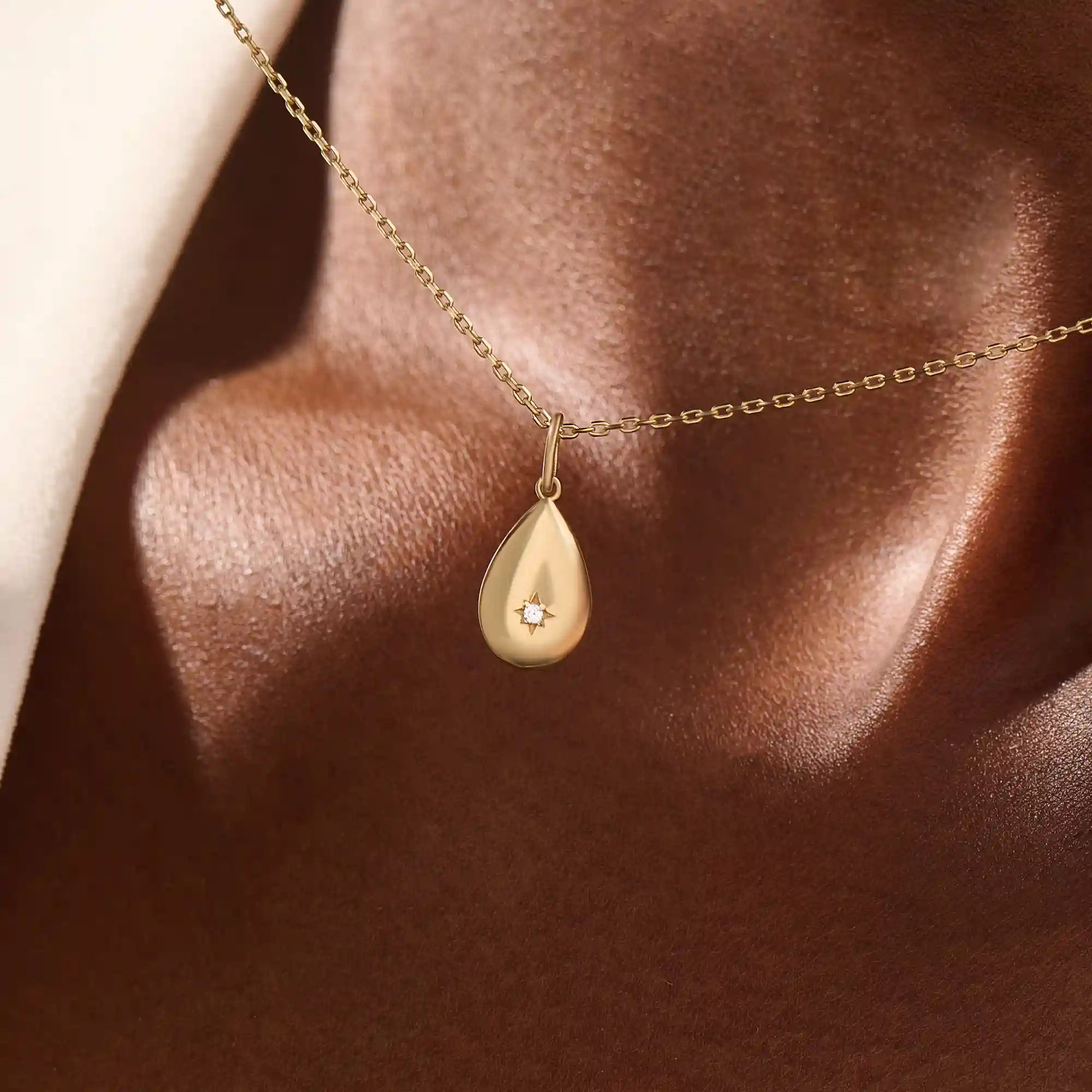Woman wearing a 14k solid gold teardrop necklace with a tiny moissanite centerpiece. Elegant and dainty gold pendant for daily style. Subtle sparkle for modern looks.