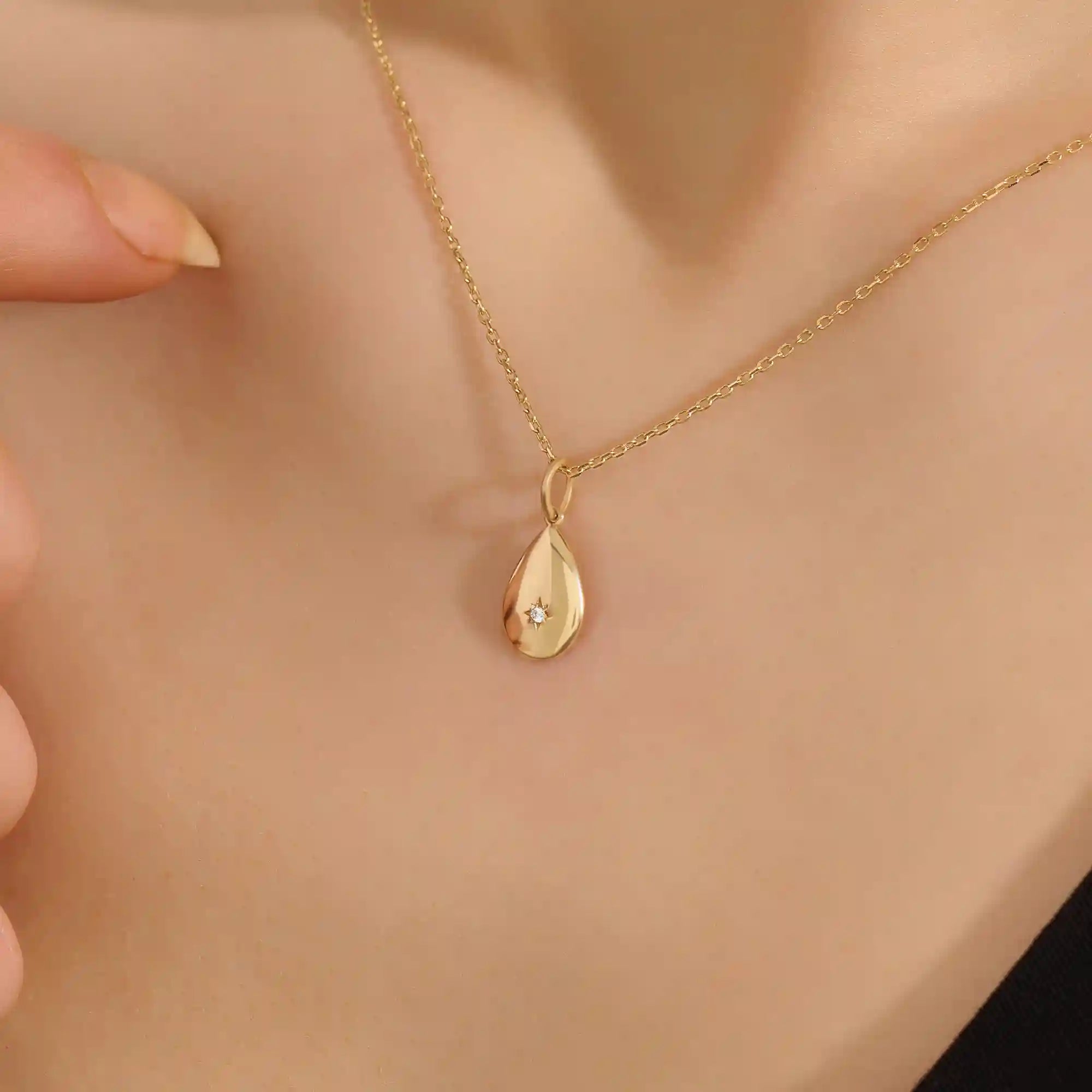 Woman wearing a 14k solid gold teardrop necklace with a tiny moissanite centerpiece. Elegant and dainty gold pendant for daily style. Subtle sparkle for modern looks.