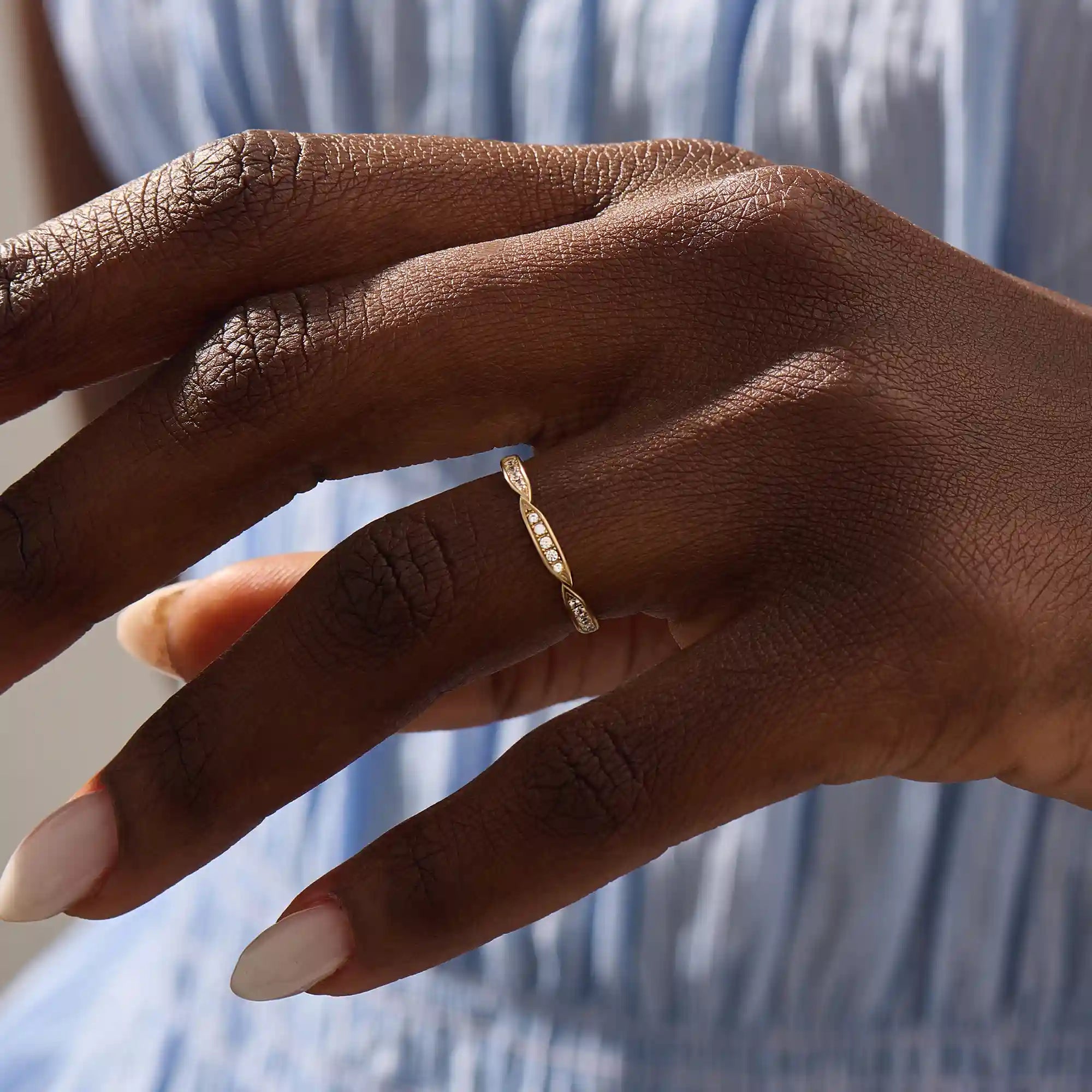Woman wearing a 14k solid yellow gold stacking wedding ring featuring marquise-inspired sections with round brilliant cut moissanite stones on her ring finger