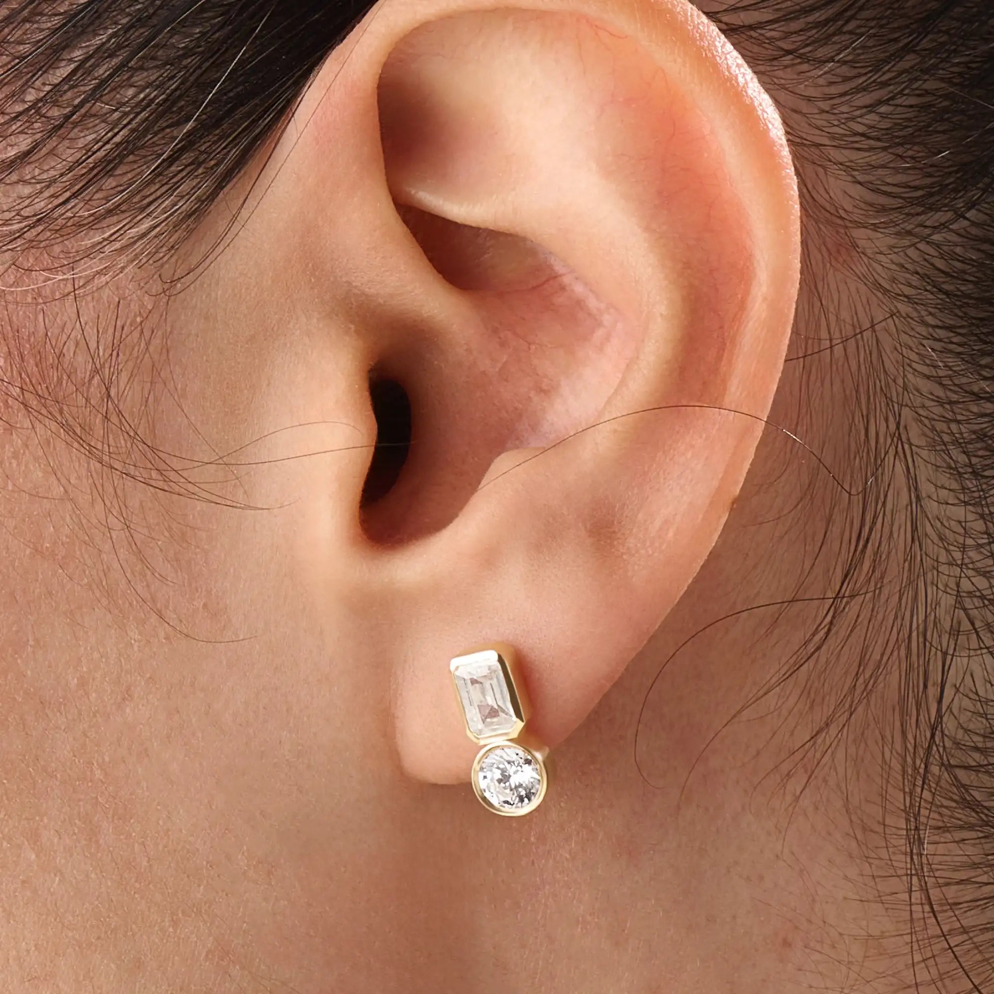 Model wearing 14k gold vermeil toi et moi stud earrings featuring a duo of emerald and round-cut stones, exuding modern sophistication with a classic touch.
