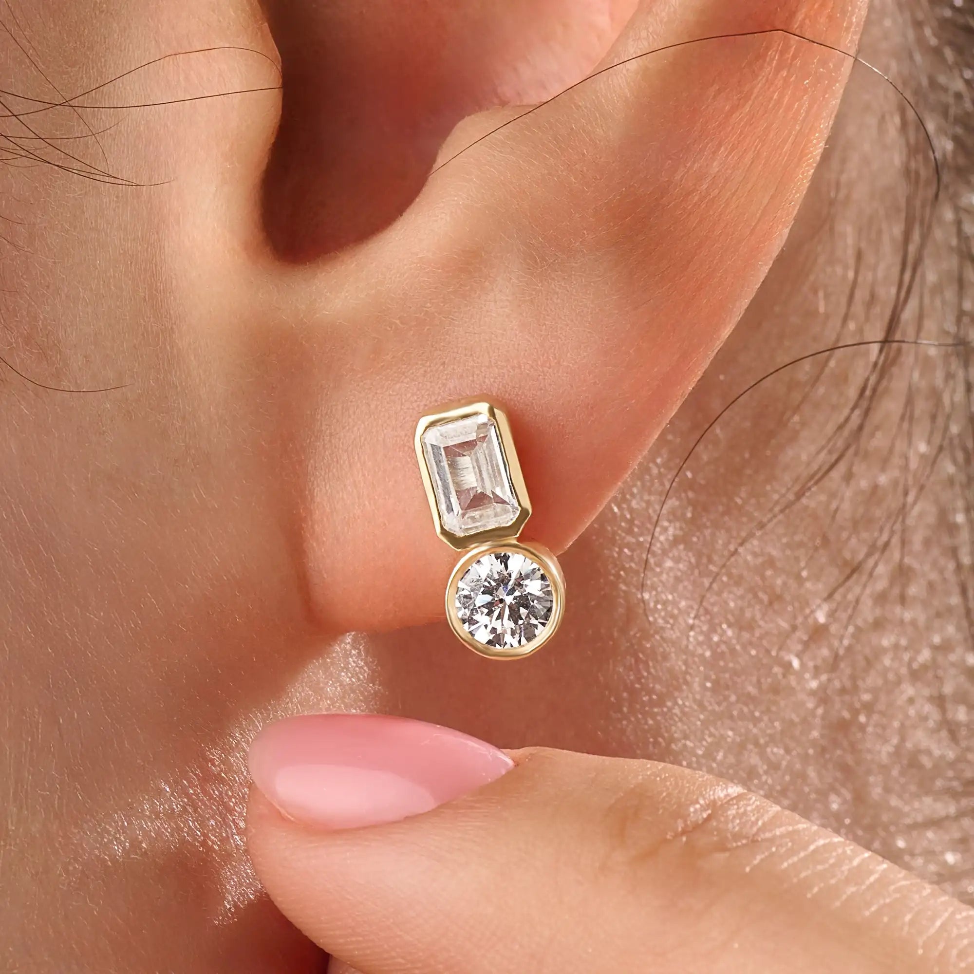 Model wearing 14k gold vermeil toi et moi stud earrings featuring a duo of emerald and round-cut stones, exuding modern sophistication with a classic touch.

