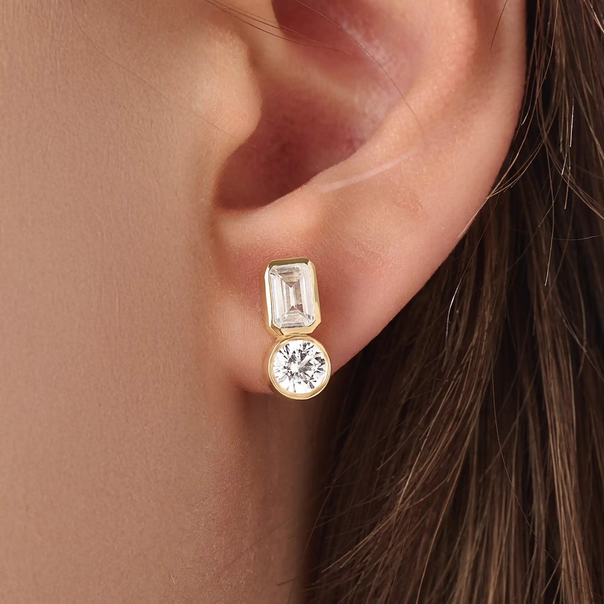 Model wearing 14k gold vermeil toi et moi stud earrings featuring a duo of emerald and round-cut stones, exuding modern sophistication with a classic touch.
