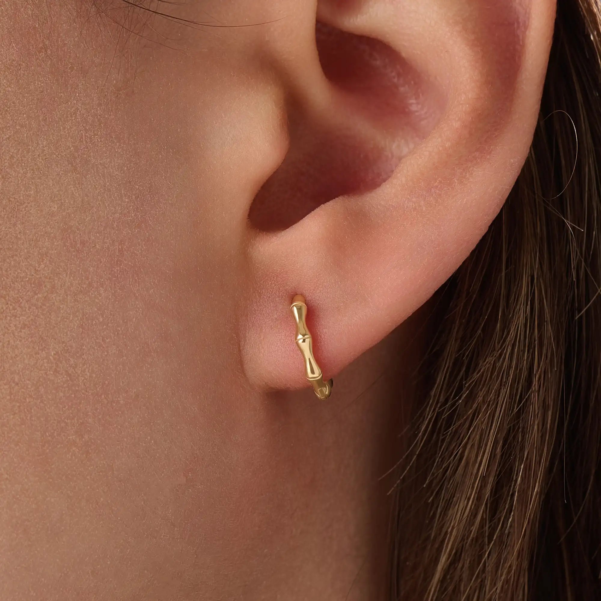 Model wearing 14k gold vermeil bone hoop earrings that highlight the sculpted, biomorphic design — a perfect mix of artistry and sophistication.
