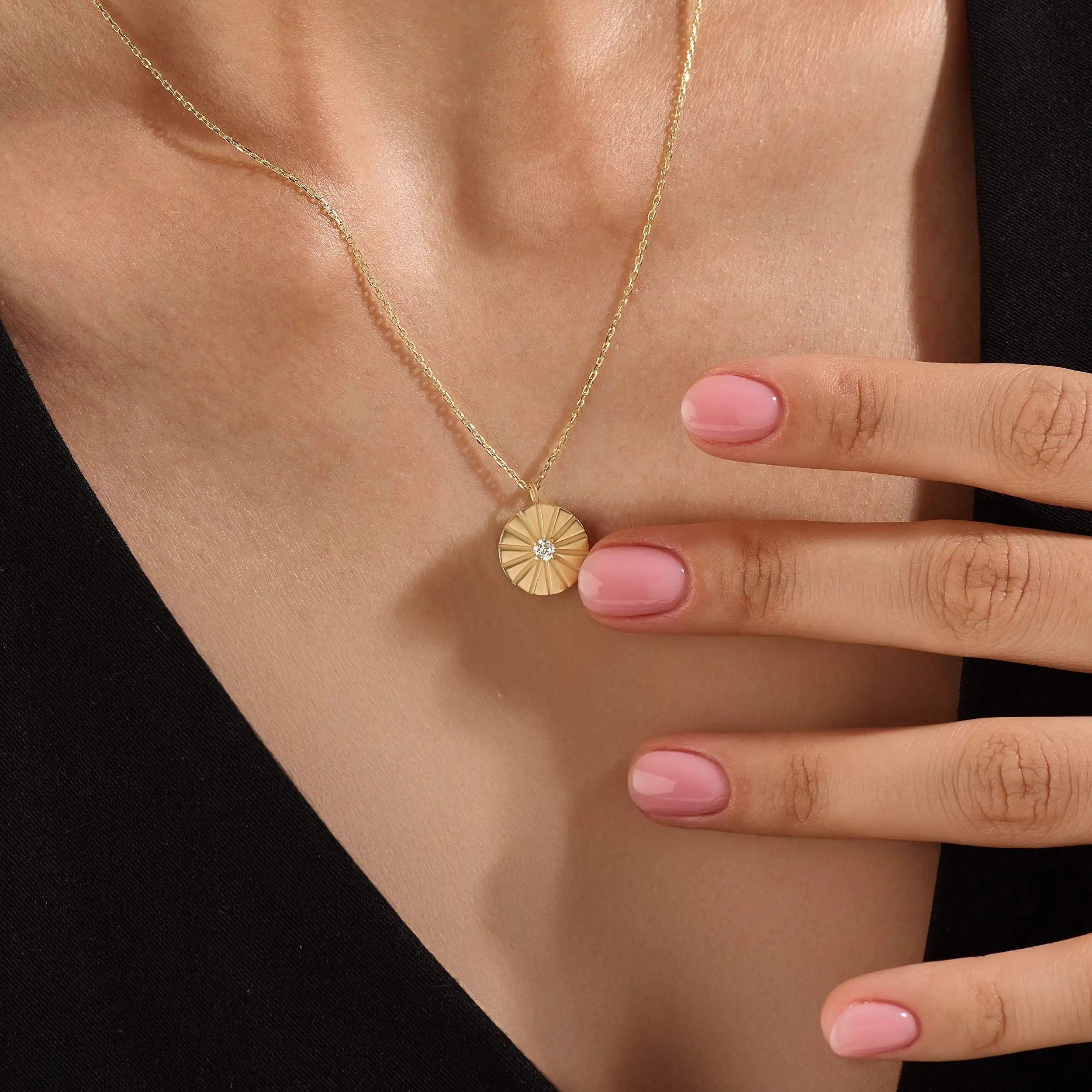 Model wearing a 14k gold vermeil coin necklace featuring a radiant engraved medallion pendant with a central cubic zirconia, adding a refined glow to any look.
