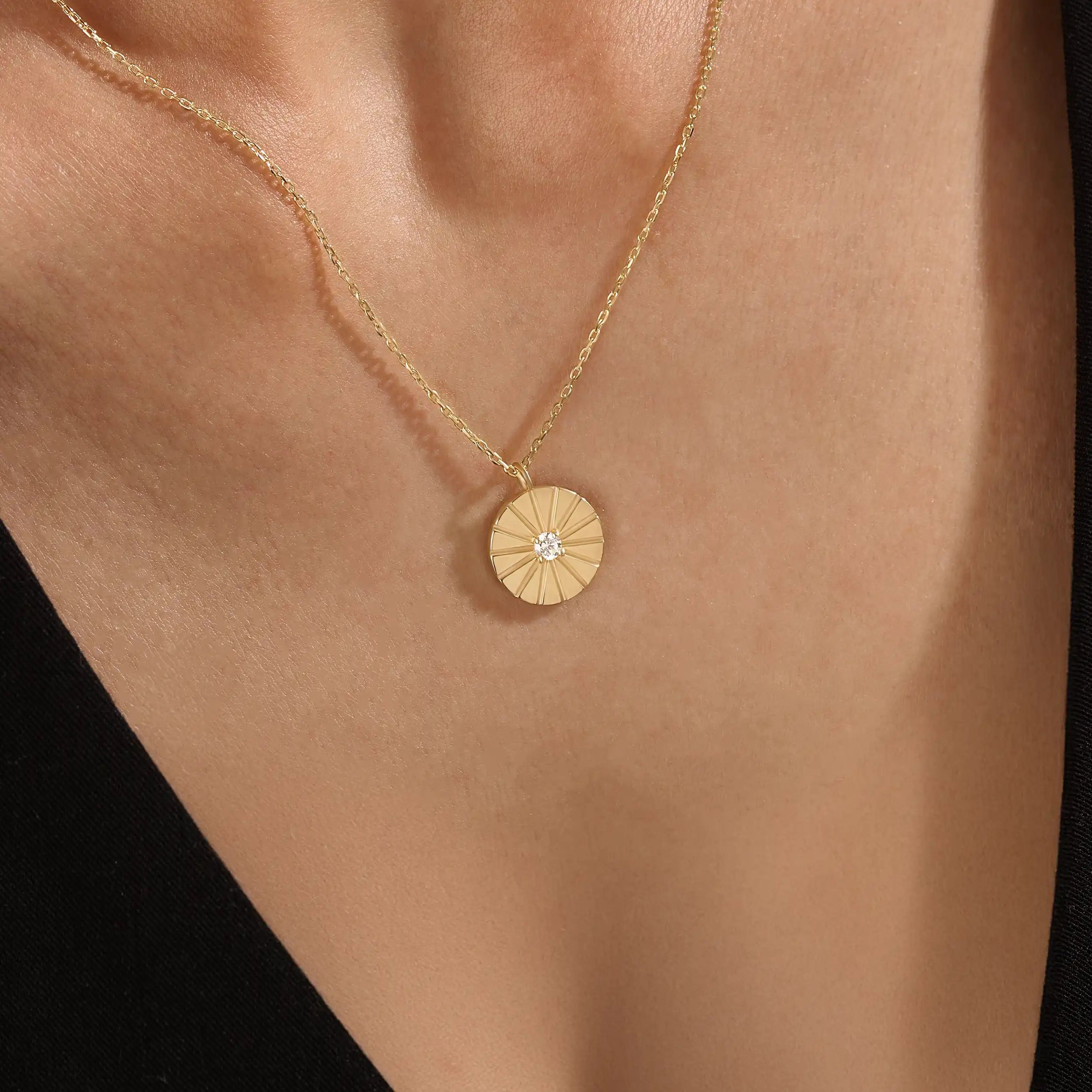Model wearing a 14k gold vermeil coin necklace featuring a radiant engraved medallion pendant with a central cubic zirconia, adding a refined glow to any look.
