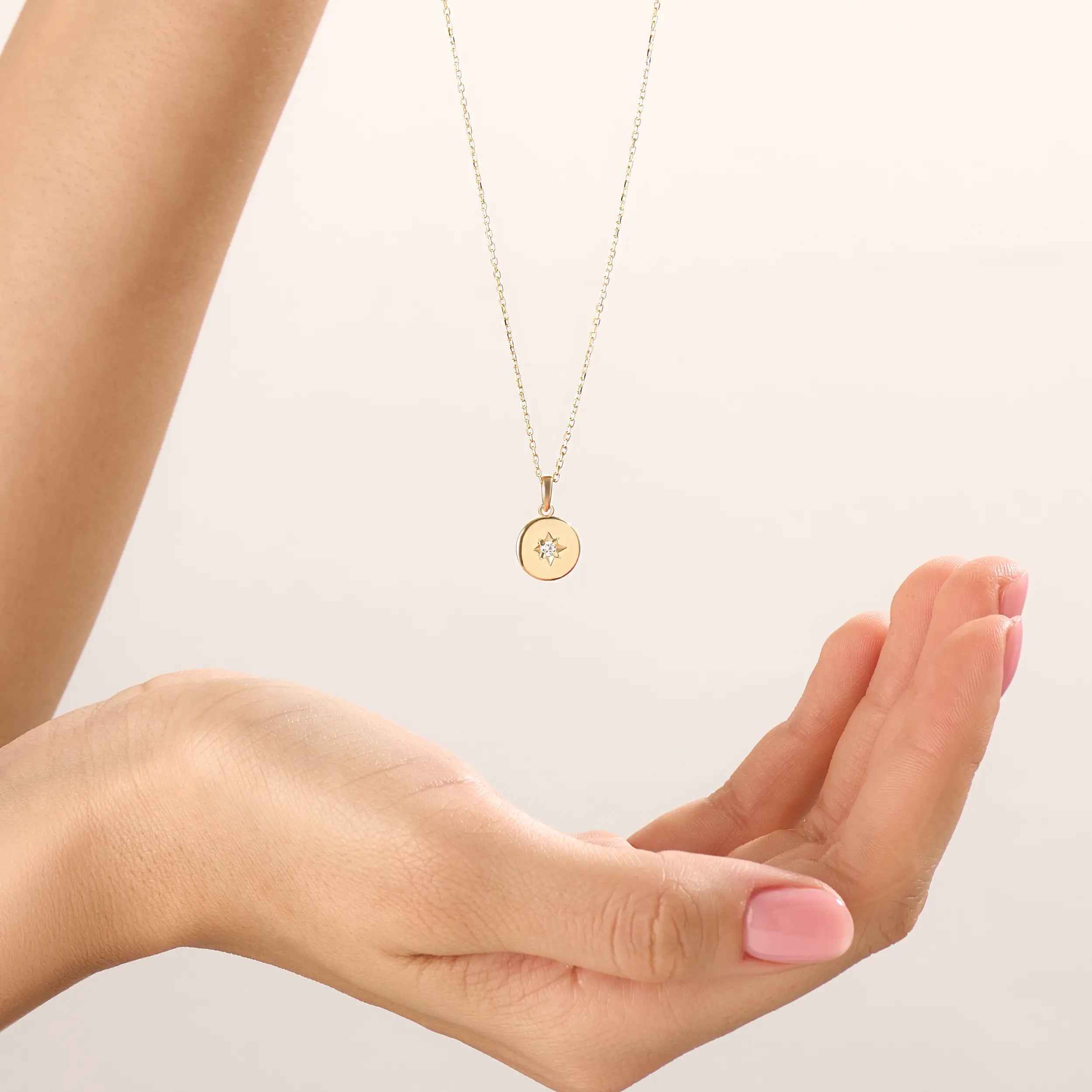 Model wearing a 14k gold vermeil starburst coin necklace featuring a minimalist round pendant with a luminous cubic zirconia centerpiece for a subtle celestial charm.
