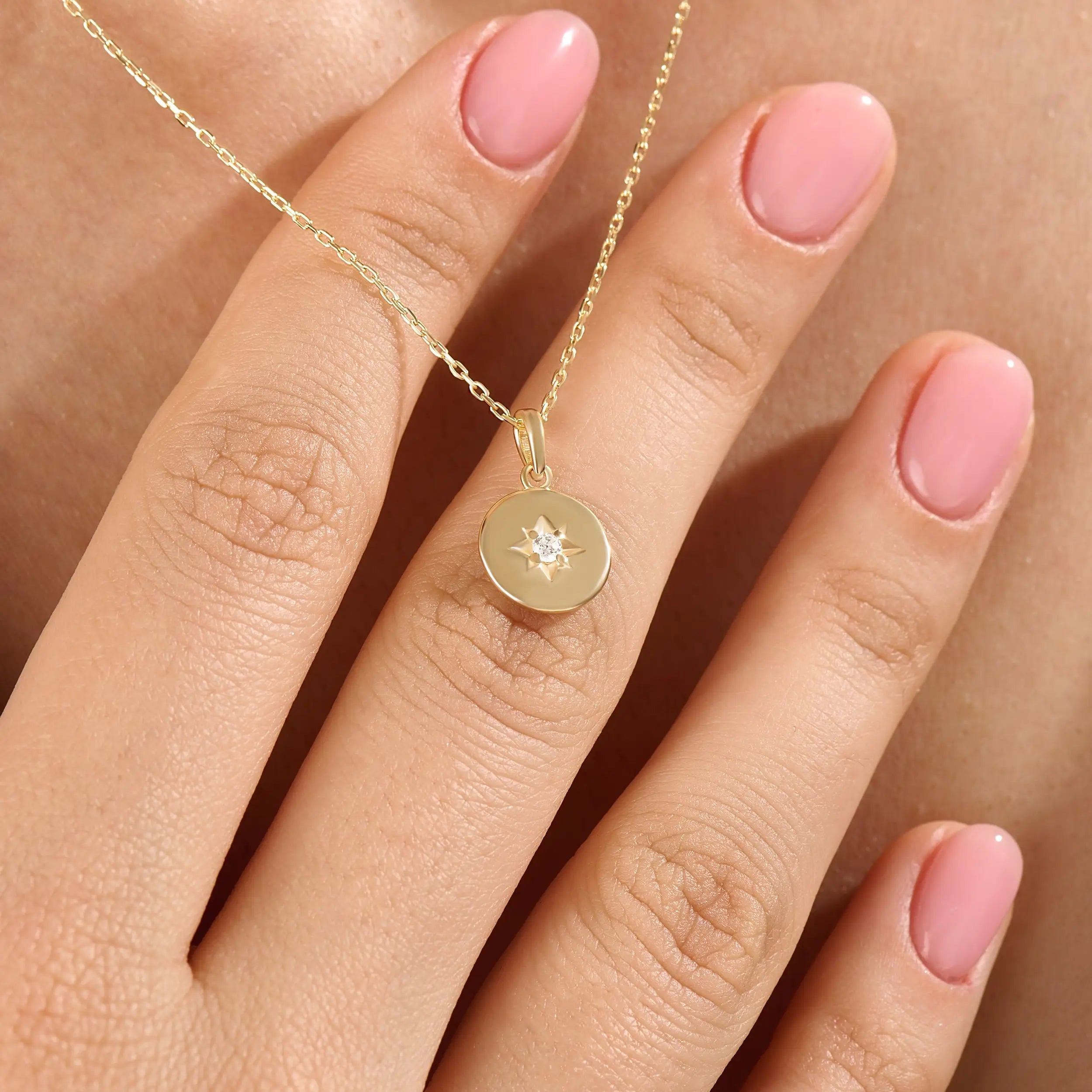 Model wearing a 14k gold vermeil starburst coin necklace featuring a minimalist round pendant with a luminous cubic zirconia centerpiece for a subtle celestial charm.
