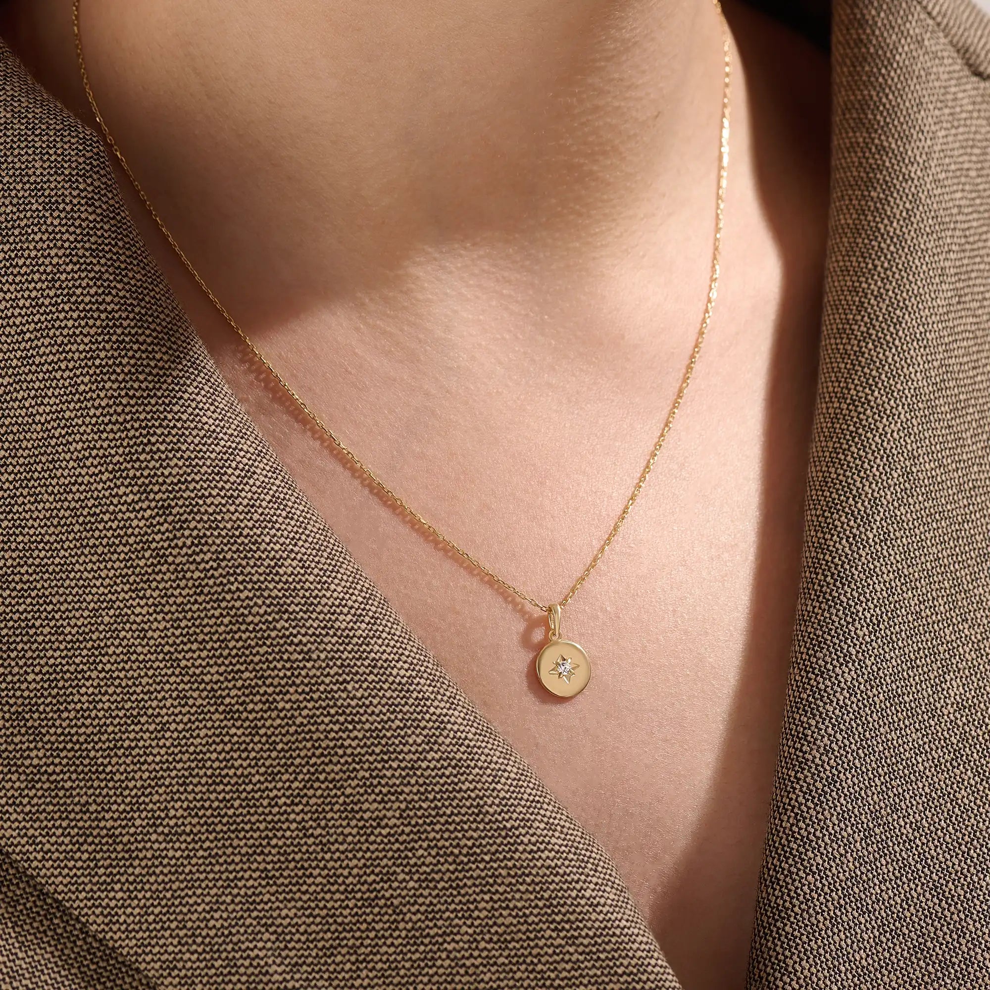 Model wearing a 14k gold vermeil starburst coin necklace featuring a minimalist round pendant with a luminous cubic zirconia centerpiece for a subtle celestial charm.
