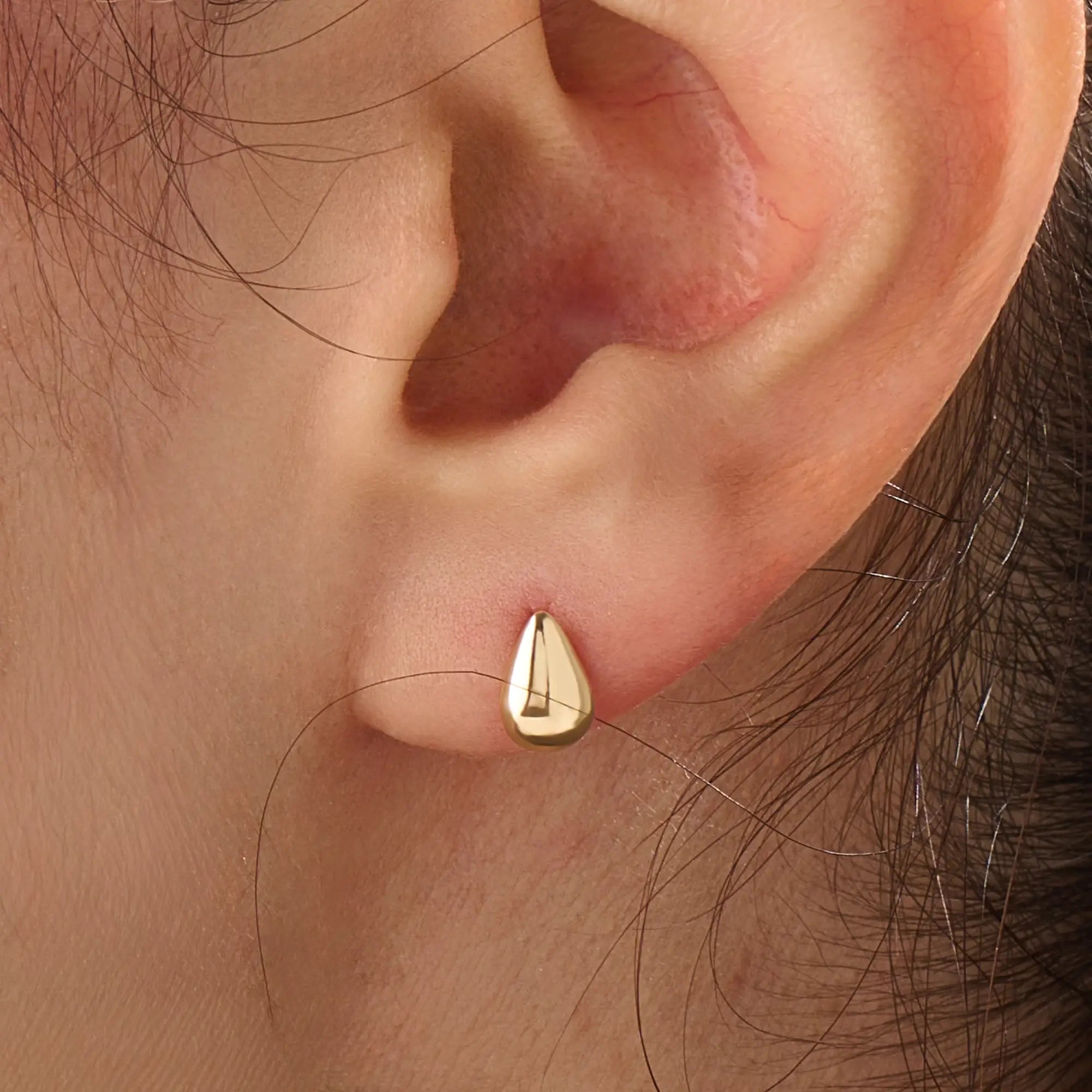 Model wearing 14k gold vermeil teardrop stud earrings that capture light with their glossy, rounded teardrop design for a sophisticated finish.
