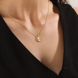 Model wearing a 14k gold vermeil textured coin necklace featuring a radiant beaded pendant with a central cubic zirconia, blending vintage charm with modern elegance.
