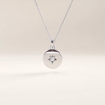 Silver vermeil starburst coin necklace with a sleek circular medallion showcasing a delicate starburst detail centered by a clear cubic zirconia stone.

